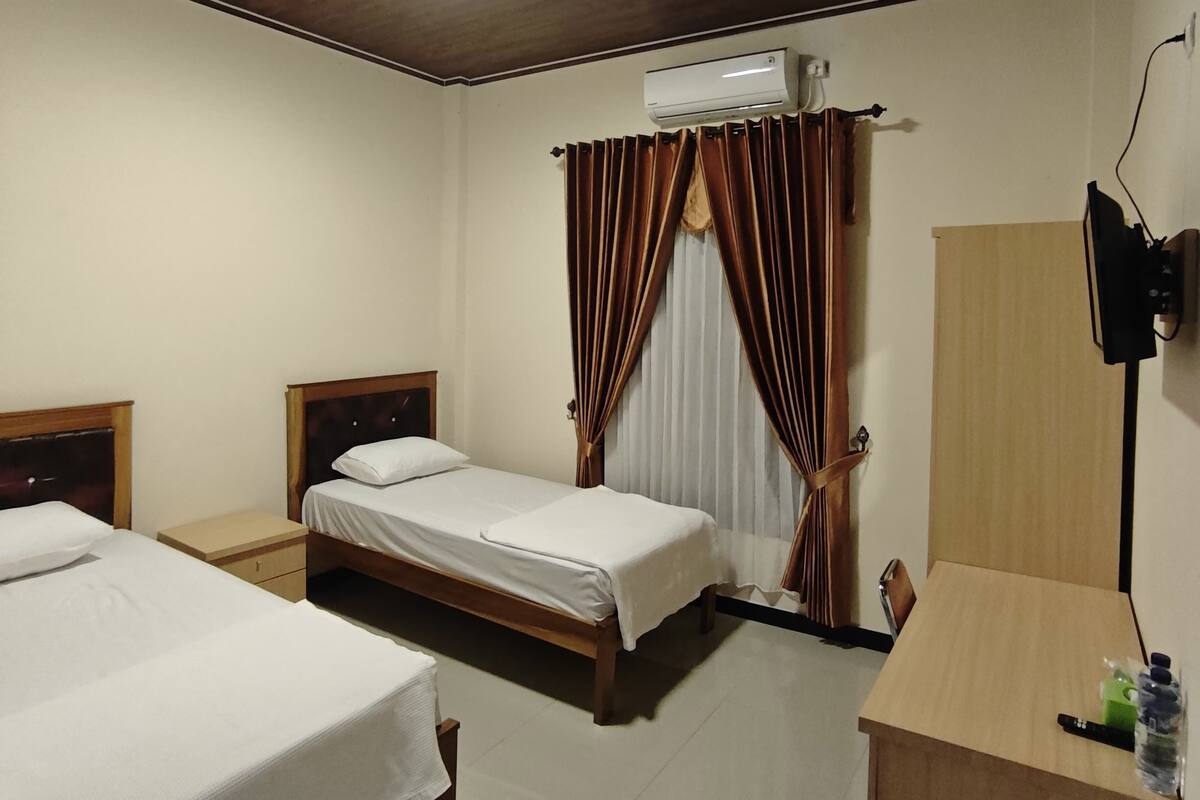 A hotel room with two beds, a desk, a chair, an air conditioning unit, and a television.