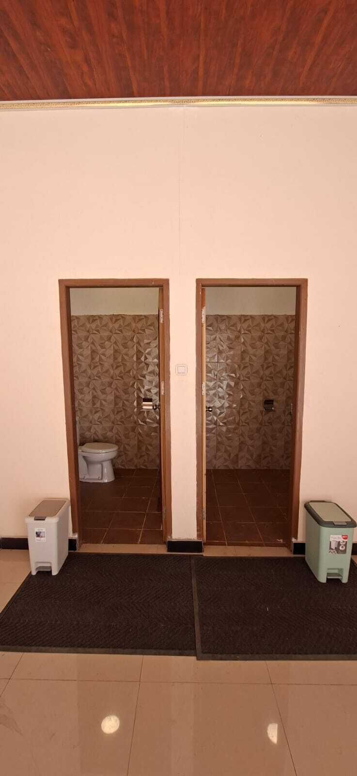 A hallway with two doors leading to bathrooms, each with a toilet and a trash bin.