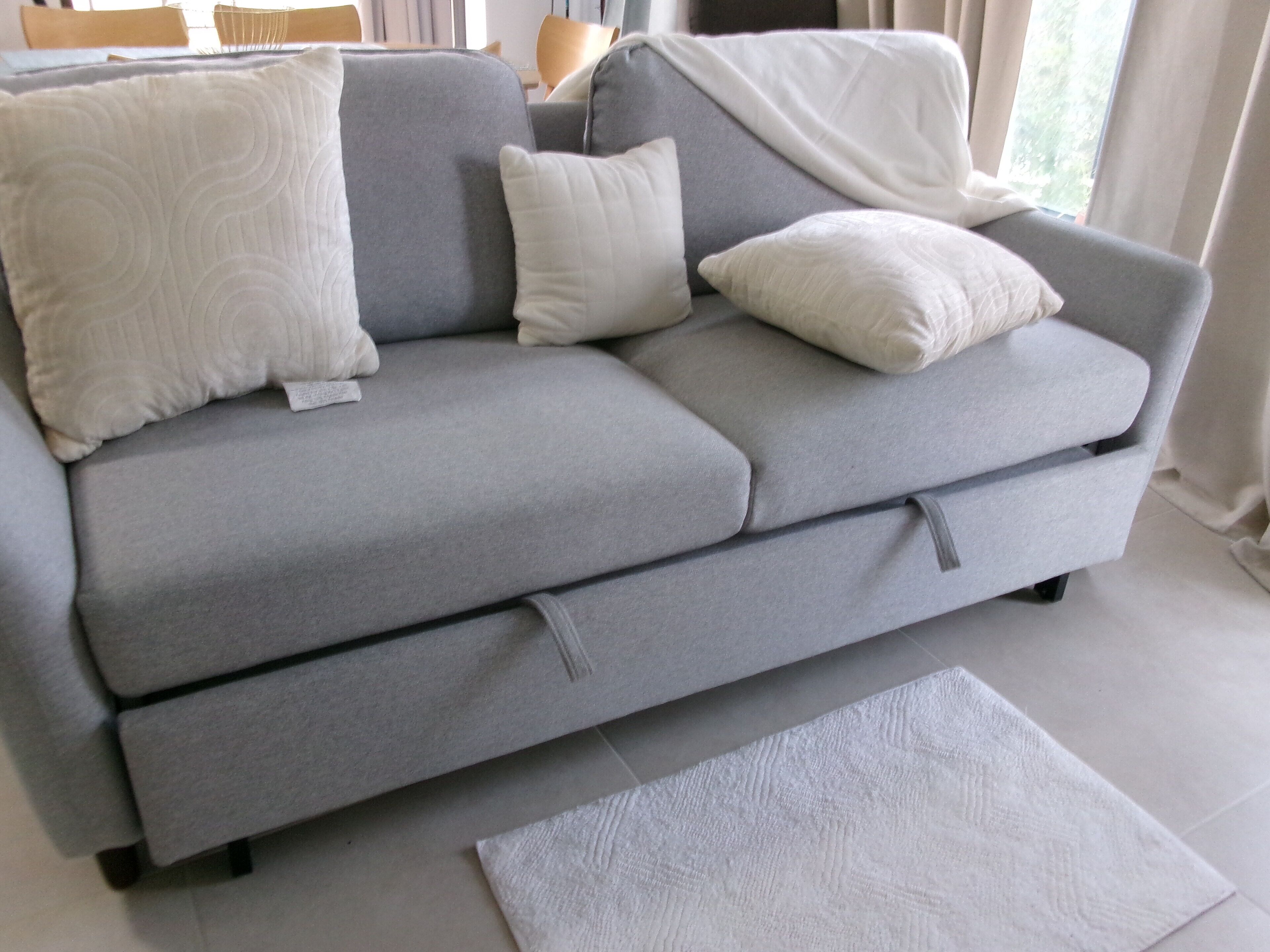 Un canapé gris avec des coussins blancs et un plaid assorti, accompagné d’un tapis blanc.