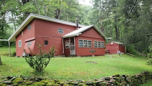 A red two-story house with a stone wall in front, surrounded by greenery.