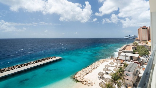 Una vista costiera con un molo, acque cristalline turchesi, una spiaggia sabbiosa e una città all'orizzonte con edifici e una nave da crociera.