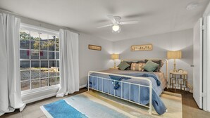 Ein Schlafzimmer mit Bett, Deckenventilator, Nachttischlampen und einem Fenster mit Vorhängen.