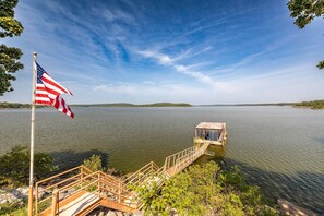 Un muelle se adentra en un lago tranquilo con una bandera estadounidense, rodeado de vegetación y un cielo despejado.