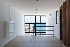 A hallway with a large window, a door, and a wall-mounted light fixture. - Majestic 602 2-Bed Ocean View Penthouse by Bocobay (Willemstad)