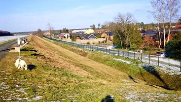Een landelijk landschap met een grashelling, een hek en huizen op de achtergrond.