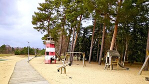 A sandy beach with a wooden boardwalk, a red and white lighthouse, and a small wooden playhouse. - Bernsteinsee Home and Ferien Forest Chalet (Sassenburg)