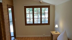 A room with a bed, a window, a nightstand with a lamp, and a brick wall. - Bernsteinsee Home and Ferien Forest Chalet (Sassenburg)