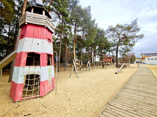 Una playa con una estructura roja y blanca, una cubierta de madera y un parque infantil.