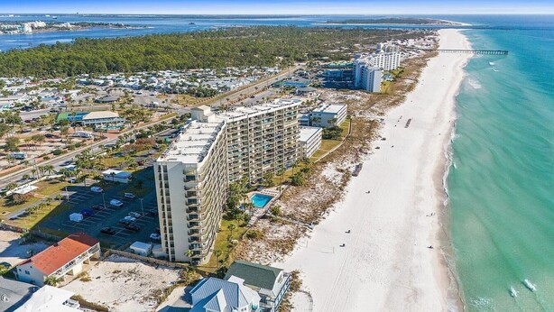 Vista aérea de una zona costera con playa, un muelle y un complejo hotelero con varios edificios.