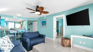 Una sala de estar con ventilador de techo, televisor y comedor con mesa y sillas.
