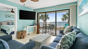 Una habitación con cama, televisión, sofá, mesa de centro y balcón con vista a la playa.