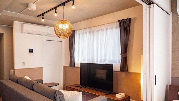 Ein modernes Hotelzimmer mit einer Couch, einem Fernseher, einem kleinen Tisch und einer Deckenleuchte.