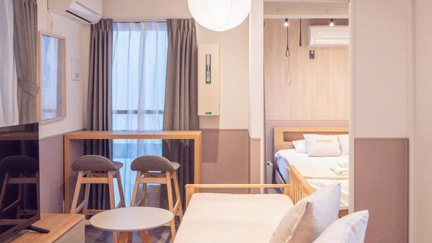 Ein modernes Hotelzimmer mit einem Holzbett, einem Schreibtisch, einem Sessel, einem Fernseher und einem großen Fenster mit Vorhängen.
