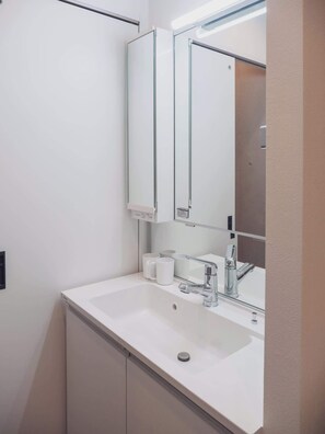 Ein modernes Badezimmer mit einem weißen Waschbecken, einem chromfarbenen Wasserhahn und einem Spiegel mit Glasrahmen.