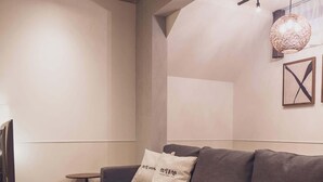 Un salon moderne avec un canapé gris, une table basse ronde, une petite table d’appoint et un luminaire suspendu.