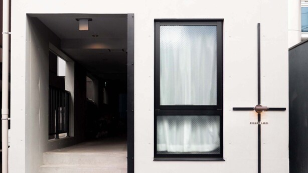 Une entrée moderne, avec un escalier menant à un intérieur sombre, une grande fenêtre avec des rideaux et un dispositif de sécurité métallique fixé au mur.