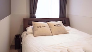 Une chambre d’hôtel comprenant un lit, deux oreillers, une fenêtre avec des rideaux, une table de chevet et un appareil de climatisation.