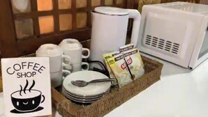 Una cafetería con una m áquina de café, tazas, un cartel, y una bandeja con platos y una cuchara.