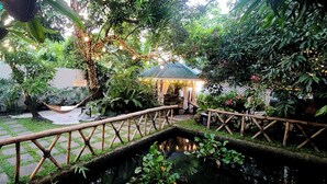 Un jardín con piscina, un puente de madera y un pabellón.
