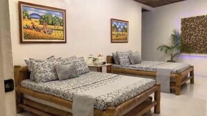 Una habitación con dos camas de madera, cada una con una colcha y almohadas a juego con estampado floral. Hay dos cuadros enmarcados en las paredes, una mesita con una lámpara y un panel decorativo.