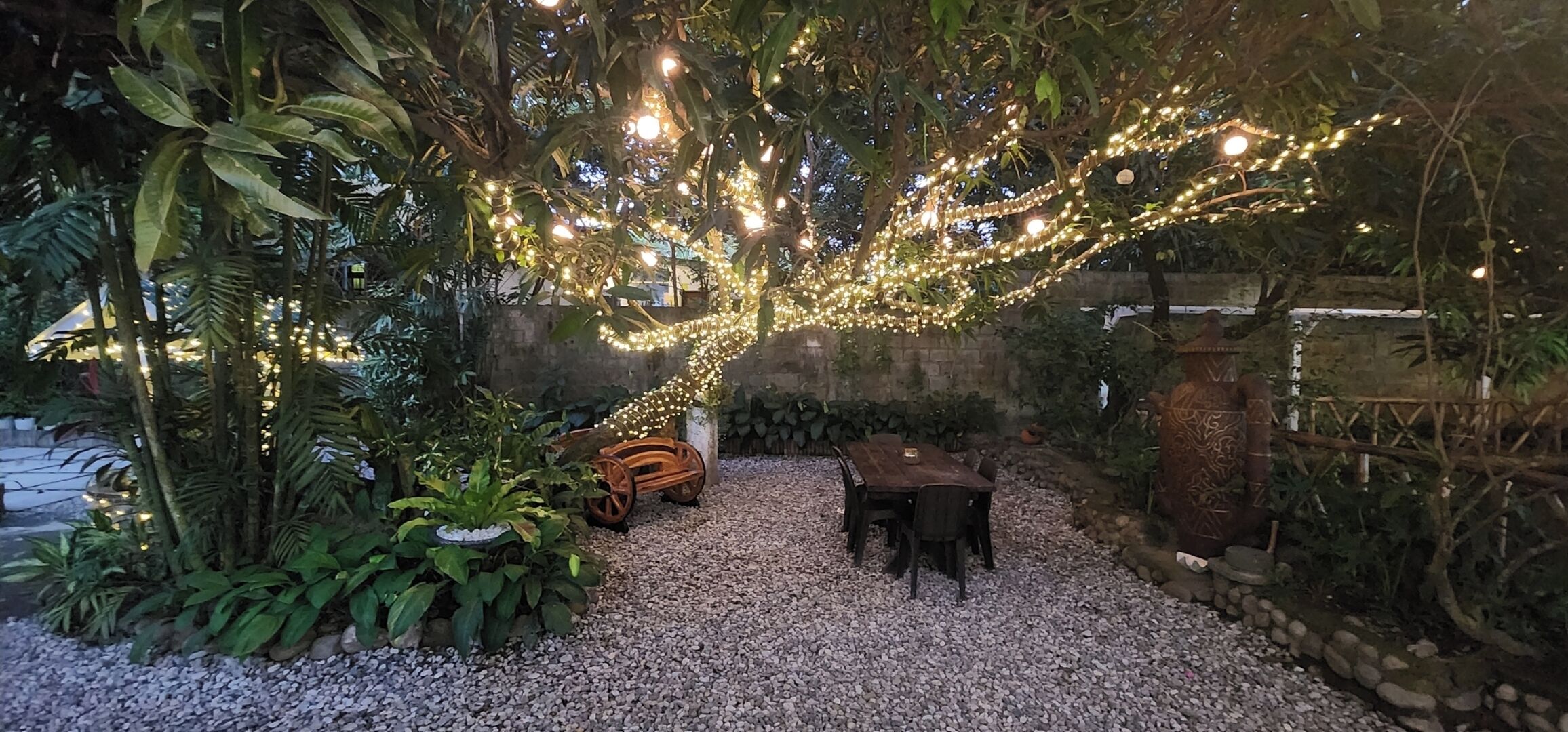 A garden with a wooden table and chairs, surrounded by plants and decorative lights.