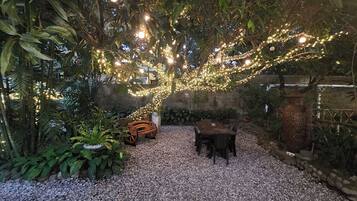 A garden with a wooden table and chairs, surrounded by plants and decorative lights.