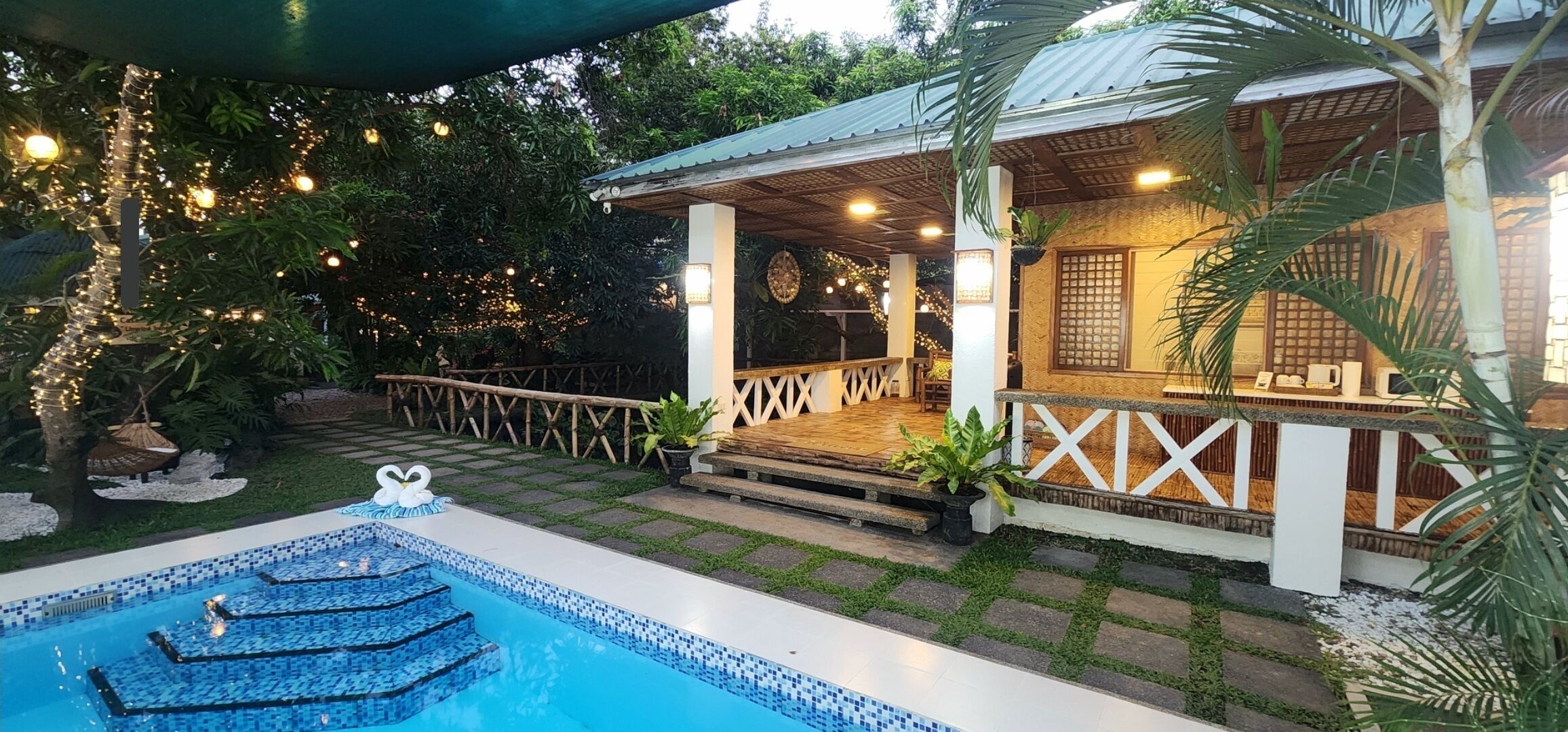 A pool area with a tiled deck, a small fountain, and a covered seating area with a railing.