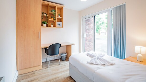 A hotel room with a bed, a desk, a chair, a wardrobe, a lamp, and a window with curtains. - Central Limerick Apartment –Bright 4BR Near Campus (Limerick)