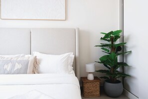 A neatly made bed with white linens, a bedside lamp, and a potted plant. - Palm View Flat at Beachvista (Dubai)