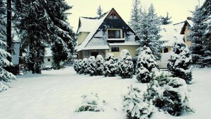 A snow-covered lodge with a prominent chimney, surrounded by snow-laden trees and a clear sky. - Pokoje Gościnne Majerczyk  (Zakopane)