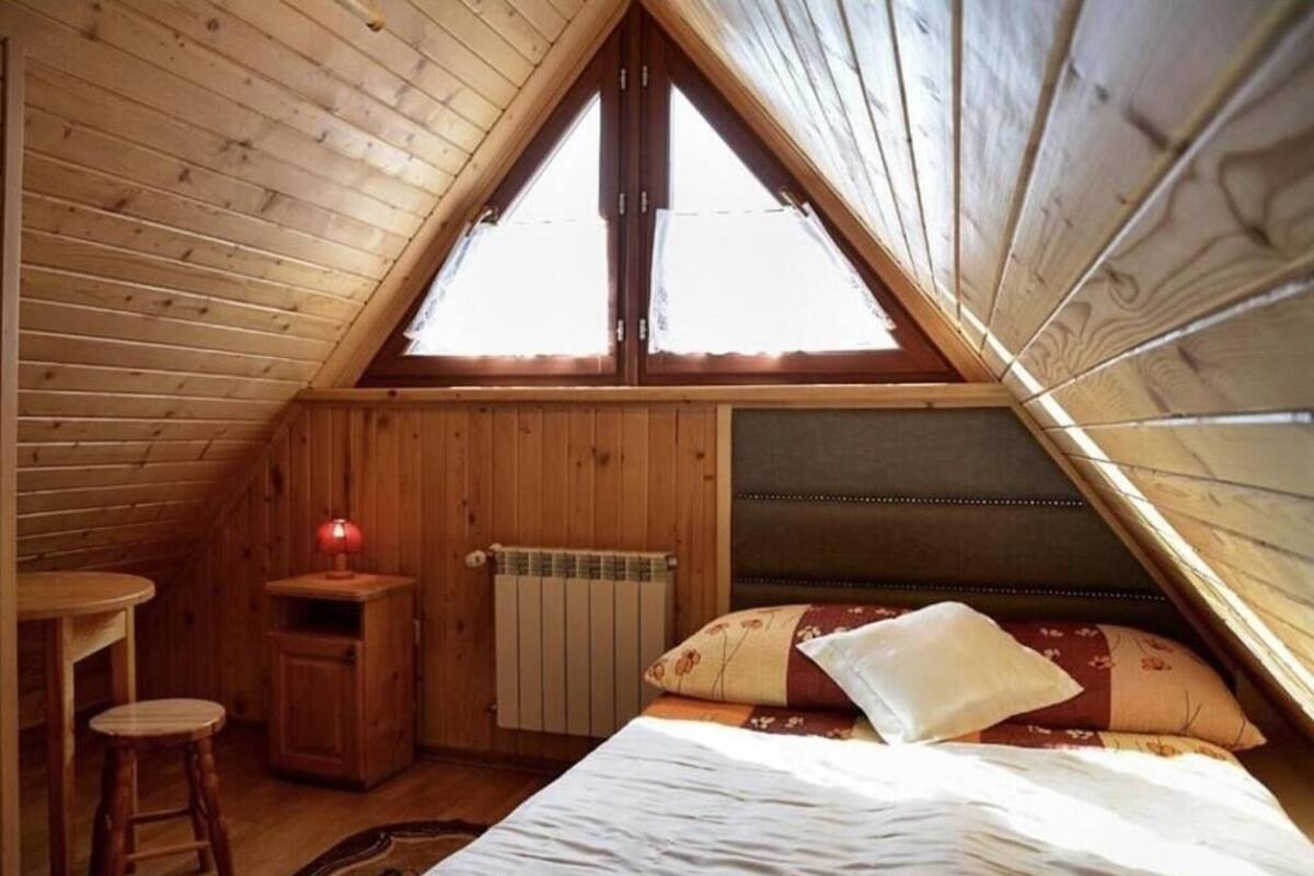 Un dormitorio acogedor en el ático, con paredes de madera, techo inclinado, una cama individual, una mesita de noche, una silla y una ventana.