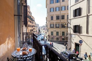 A narrow street with buildings on either side, a pedestrian crossing, and a table with food and drinks. - Modern 2-Room Apartment on the Spanish Steps • Trinity Domus (Roma)