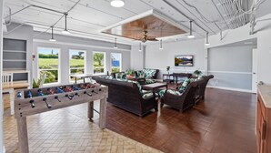 Amplia sala de estar con mesa de fútbol de mesa, asientos cómodos, ventanas grandes y ventilador de techo.