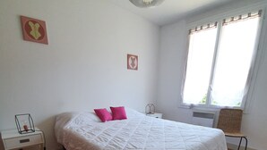 A bedroom with a bed, a bedside table, a hanging light fixture, and a window with curtains. - Vacation home on the Bay of Arcachon (La Teste-de-Buch)