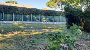 A grassy outdoor area with a hedge, a tree, and a building with large windows in the background. - Vacation home on the Bay of Arcachon (La Teste-de-Buch)