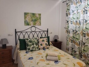 A bed with a floral bedspread, a green pillow, and a tropical leaf-patterned pillow. There are two bedside tables with lamps. - Perfect Getaway in Vera (Vera)