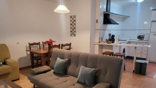 Sala de estar com sofá, mesa de jantar, cadeiras, área de cozinha com micro-ondas e luminária pendente.