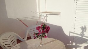 Uma mesa branca e redonda com um vaso de flores cor-de-rosa, rodeada por cadeiras de plástico brancas.