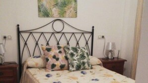 Quarto com cama, mesa de cabeceira, abajur, pintura na parede e piso de madeira.