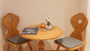 A wooden table with two chairs, a framed picture on the wall, and a book and candle on the table.