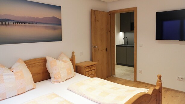 A bedroom with a bed, pillows, a nightstand, a wooden wardrobe, a painting, and a TV.