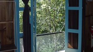 Une porte ouverte donnant sur un balcon d’où l’on peut admirer les arbres et les collines.