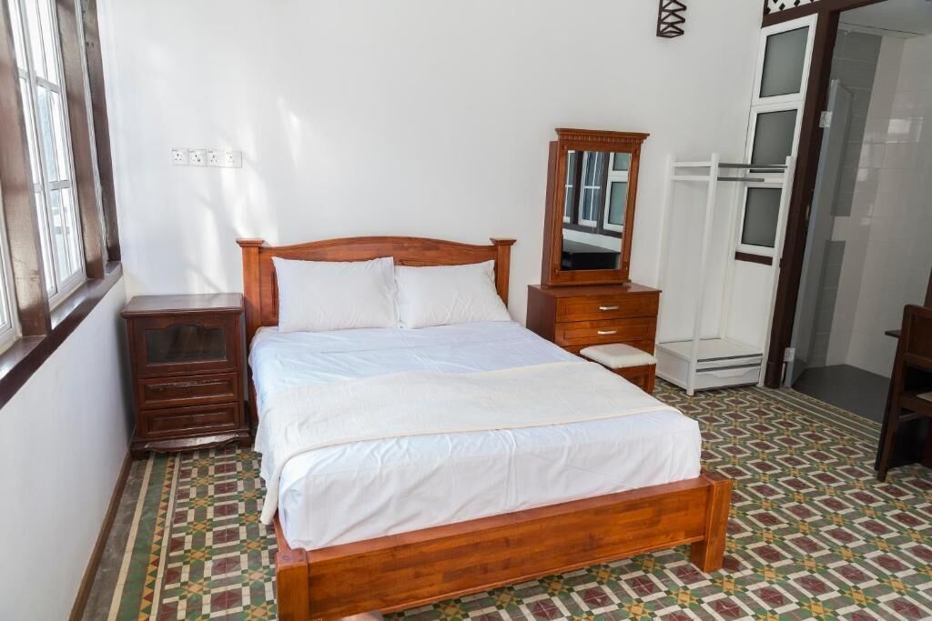 Un dormitorio con cama de madera, una mesita de noche, un aparador, un espejo y piso con diseño.