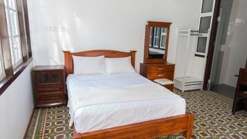 Un dormitorio con cama de madera, una mesita de noche, un aparador, un espejo y piso con diseño.