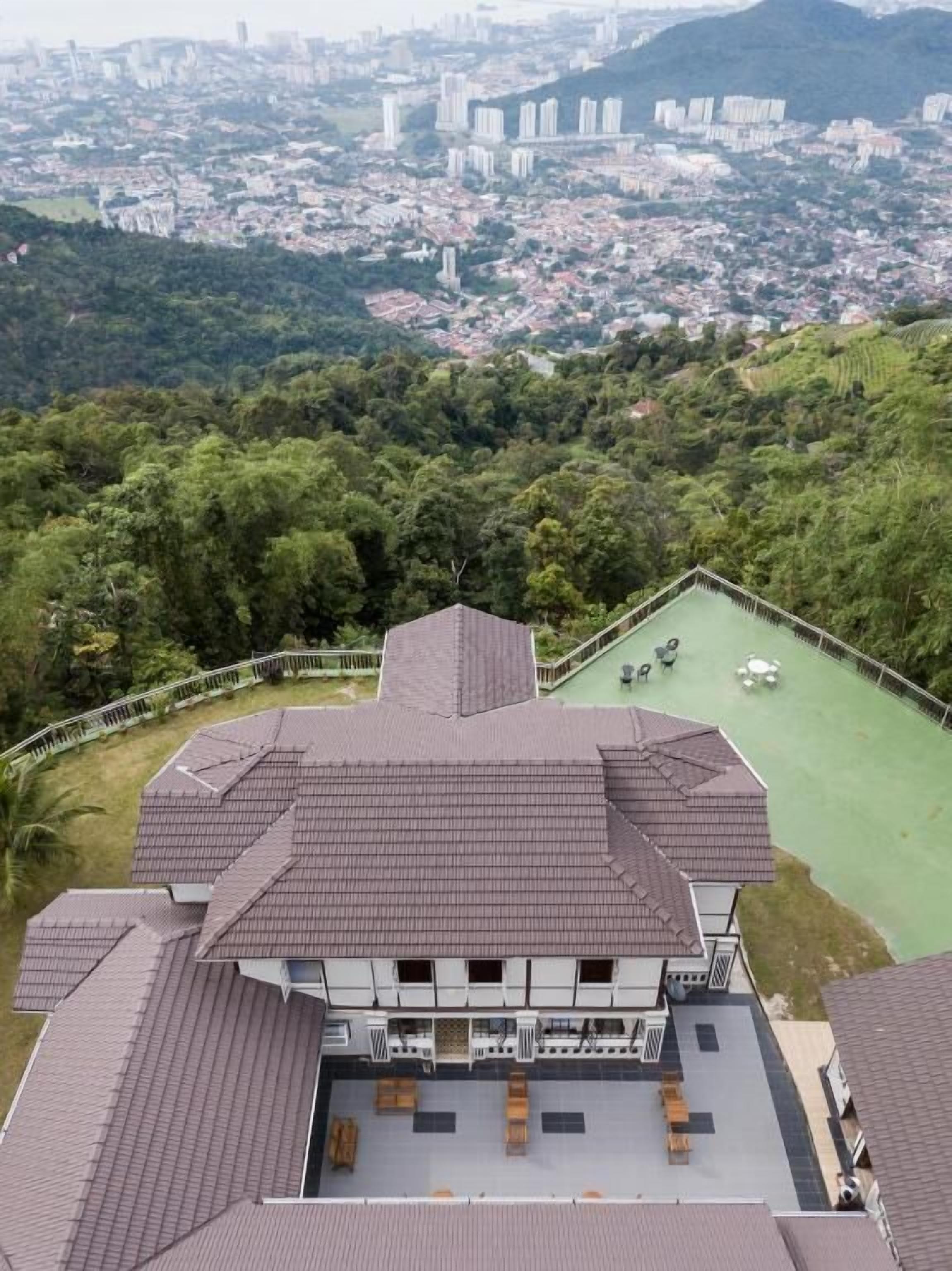 Un immeuble à plusieurs étages, doté d’un toit plat, d’une terrasse sur le toit avec des sièges, et offrant une vue sur le paysage urbain et la végétation environnante.
