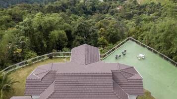 Un immeuble à plusieurs étages, doté d’un toit plat, d’une terrasse sur le toit avec des sièges, et offrant une vue sur le paysage urbain et la végétation environnante.