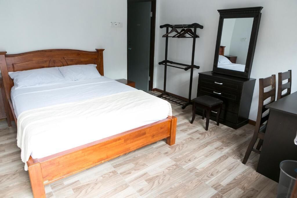 Ein Schlafzimmer mit einem hölzernen Bett, einer schwarzen Kommode, einem Spiegel und einem Kleiderständer.