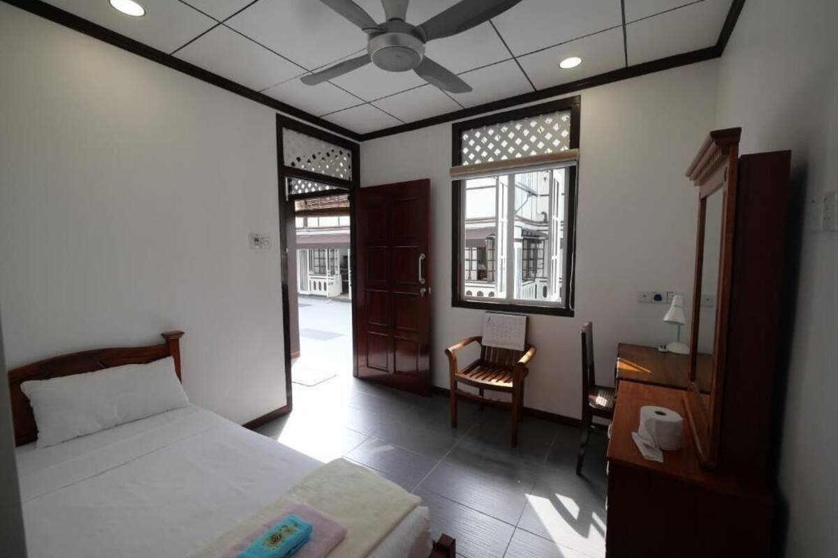 Une chambre d’hôtel avec un lit, un ventilateur de plafond, une fenêtre donnant sur un paysage agréable, une chaise et un miroir.