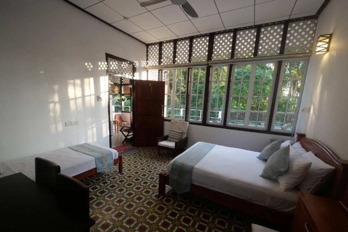 Une chambre d’hôtel avec deux lits, un bureau, une chaise et une vue sur la verdure grâce à de grandes fenêtres.