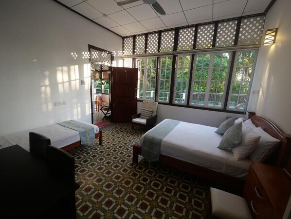Une chambre d’hôtel avec deux lits, un bureau, une chaise et une vue sur la verdure grâce à de grandes fenêtres.